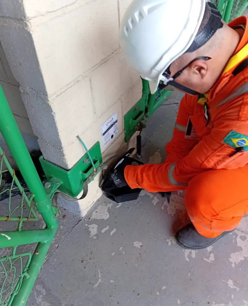 Técnico da PJO de macacão e capacete no controle de roedores junto a uma grade