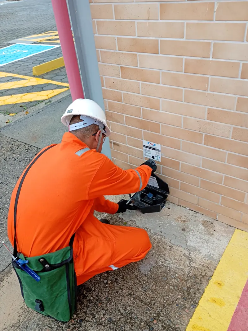 Técnico da PJO verificando porta-isca junto à parede de um prédio comercial